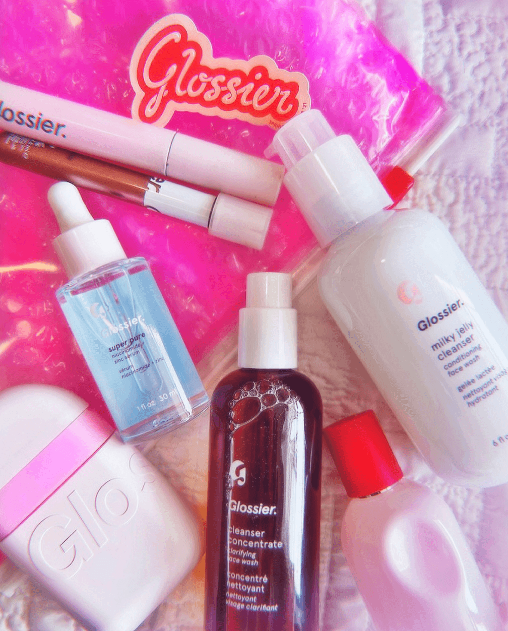 Image of seven Glossier Products laying out on pink packaging with a Glossier Sticker