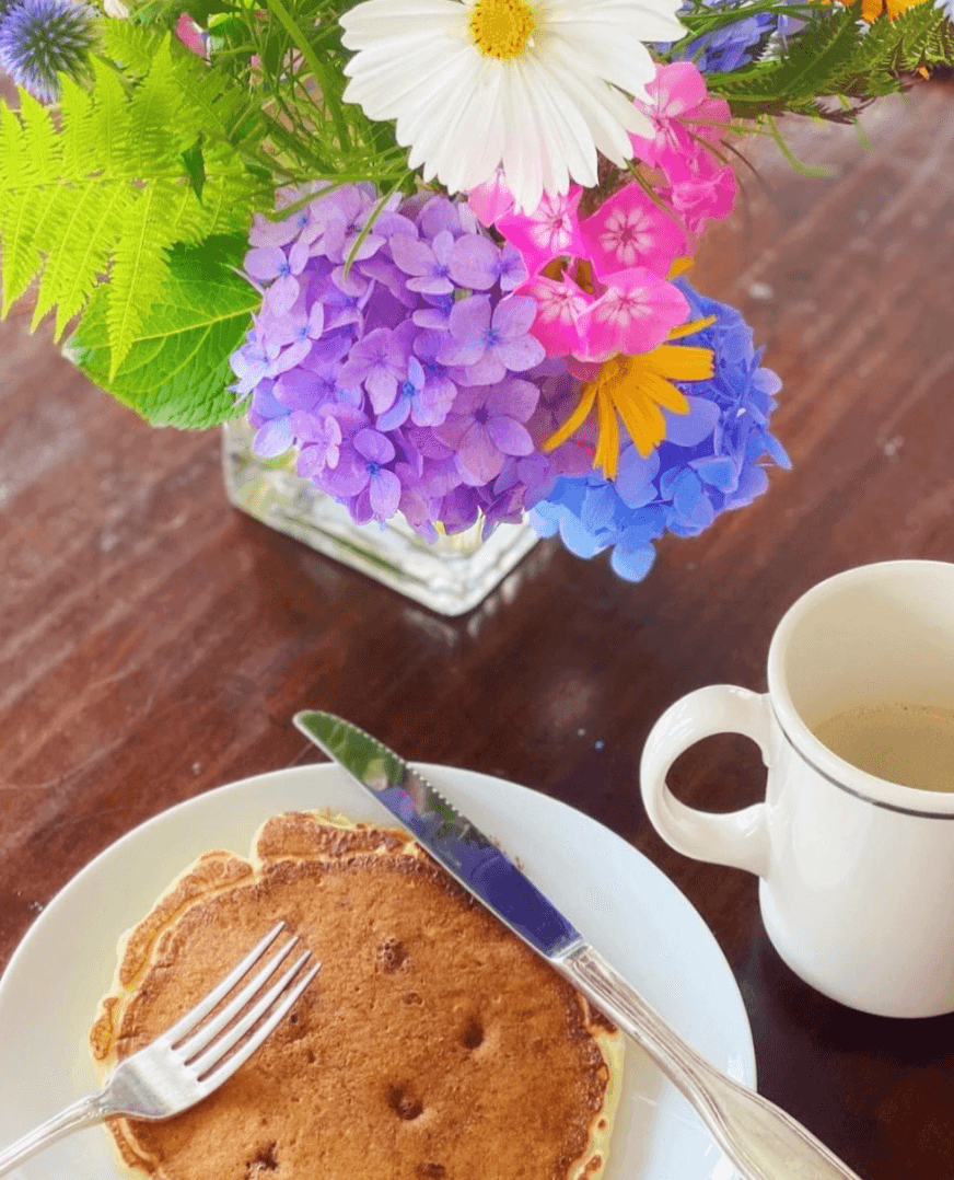 Image of coffee next to breakfast meal and floral arrangement