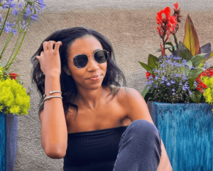 Image of Sara Sitting next to flowers in sunglasses and a crop top 